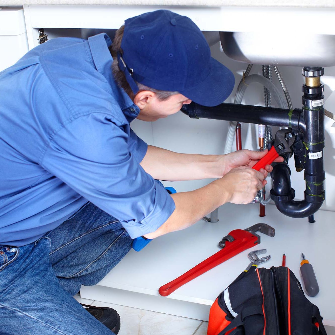 Mature plumber fixing a sink at kitchen